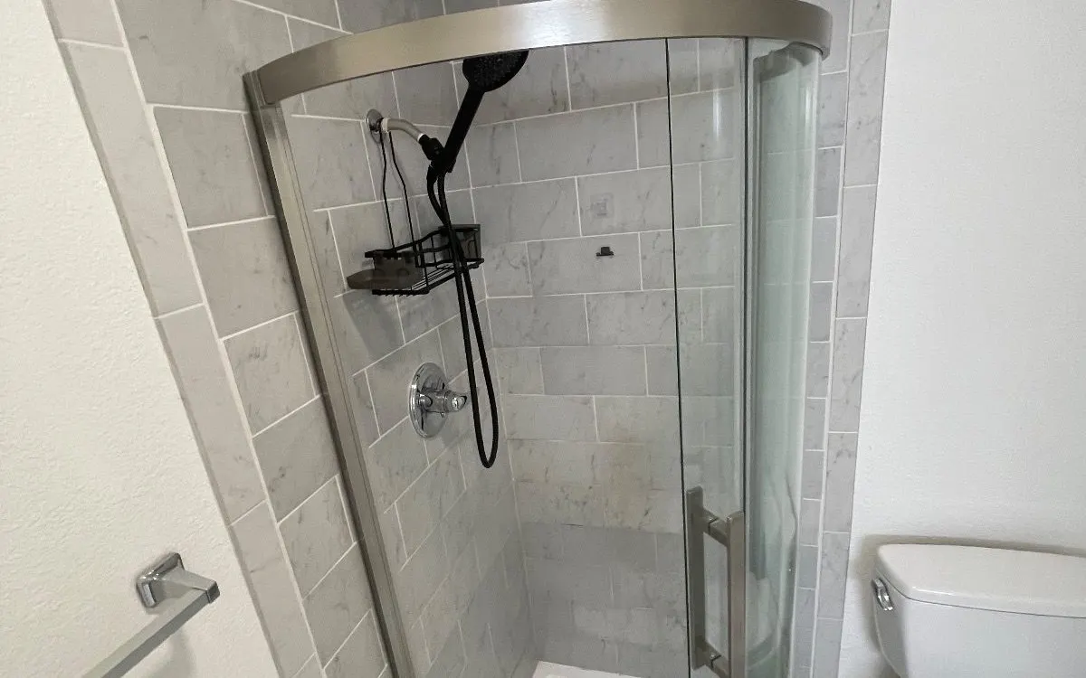 Clean corner shower with curved glass door and gray tile
