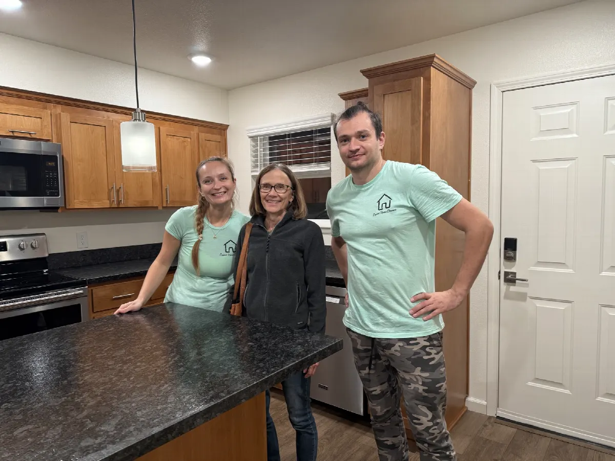Two Expert Home cleaners in branded t-shirts standing with a client at a kitchen island in a renovated home