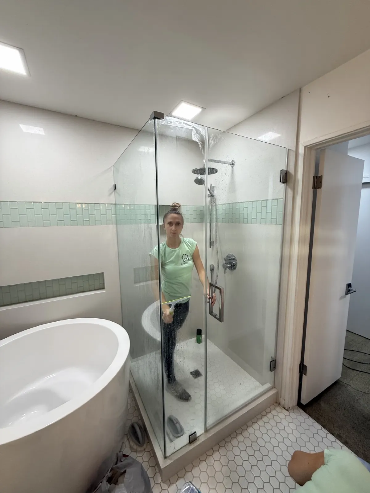 Crew member squeegeeing a new shower glass door after post-construction cleanup