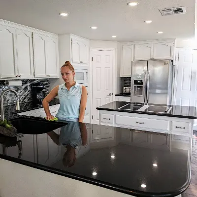 Cleaner polishing a black granite countertop in a white kitchen