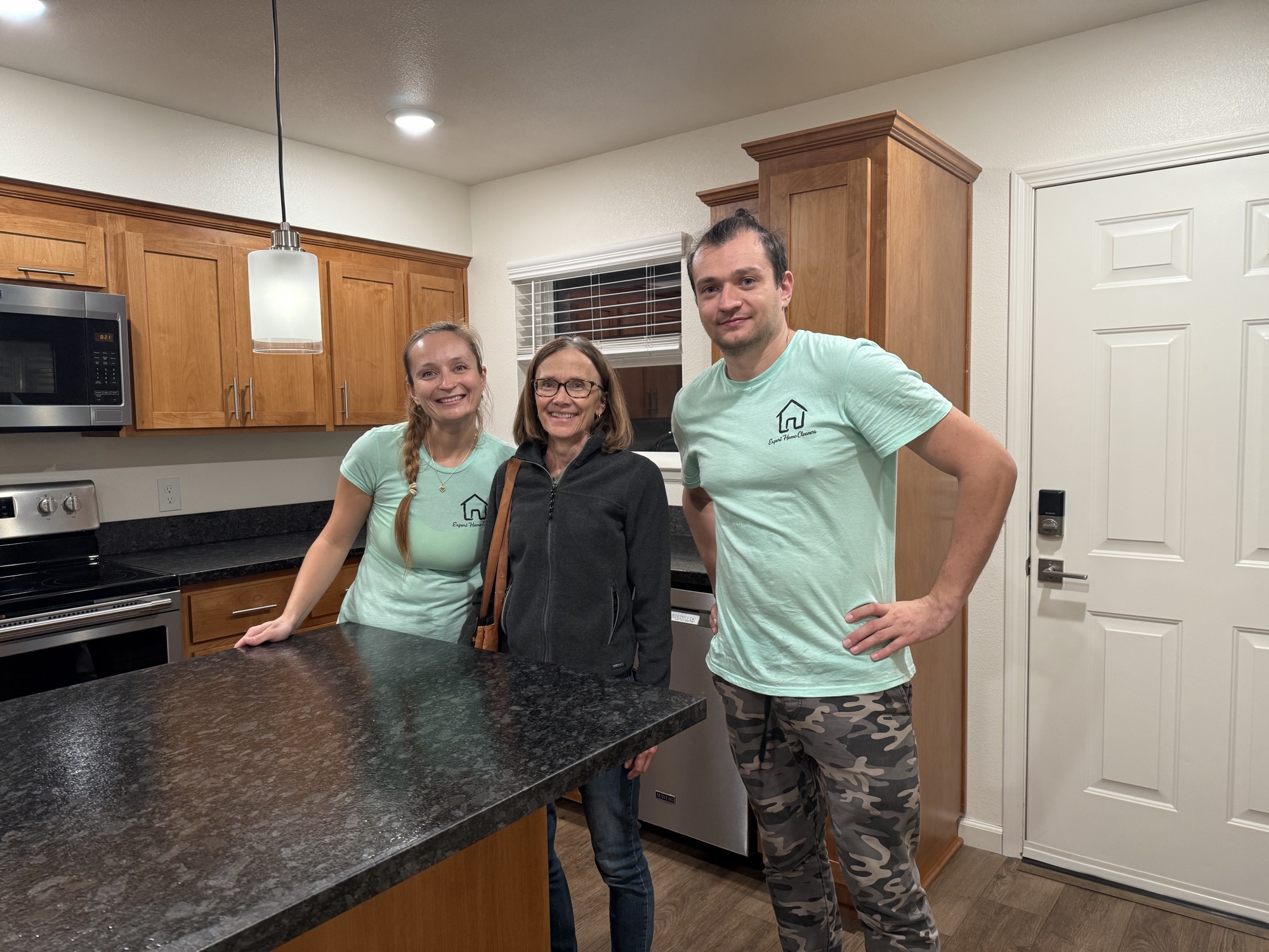 Two cleaners in branded t-shirts standing with a client at a kitchen island in a newly renovated home