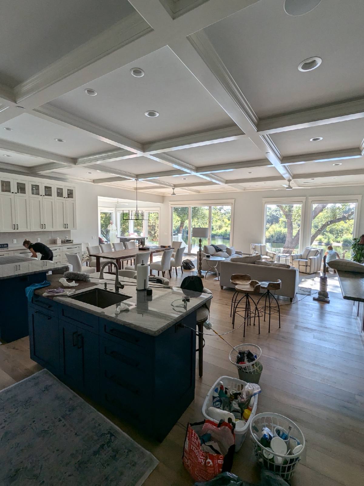 Two cleaners working through an open-plan kitchen and living room, supply caddies on the floor