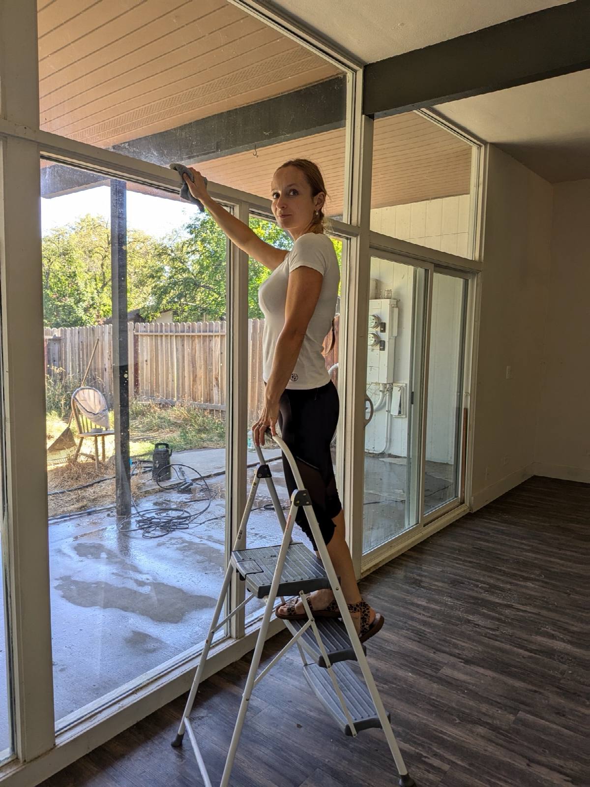 Cleaner on a step ladder wiping the top of floor-to-ceiling glass doors in an empty home