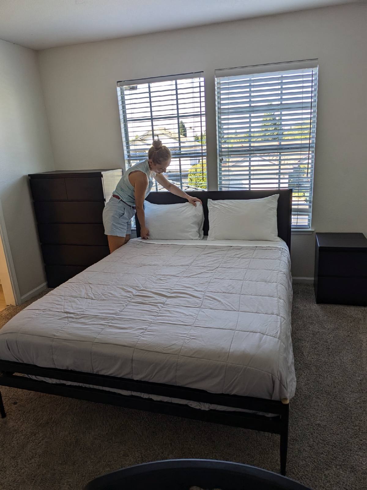 Cleaner straightening pillows and making up the bed in a carpeted bedroom