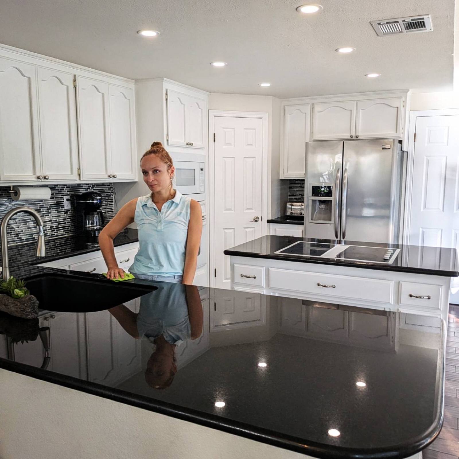 Cleaner polishing a black granite countertop in a bright white kitchen