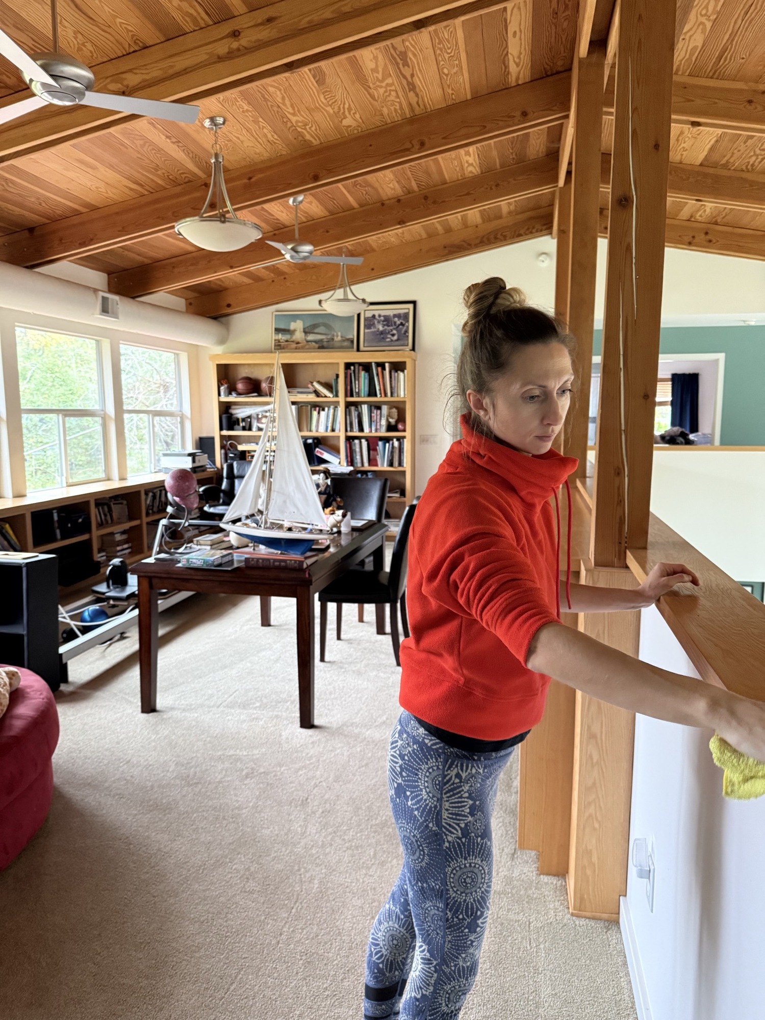 A cleaner on a ladder dusting exposed ceiling beams