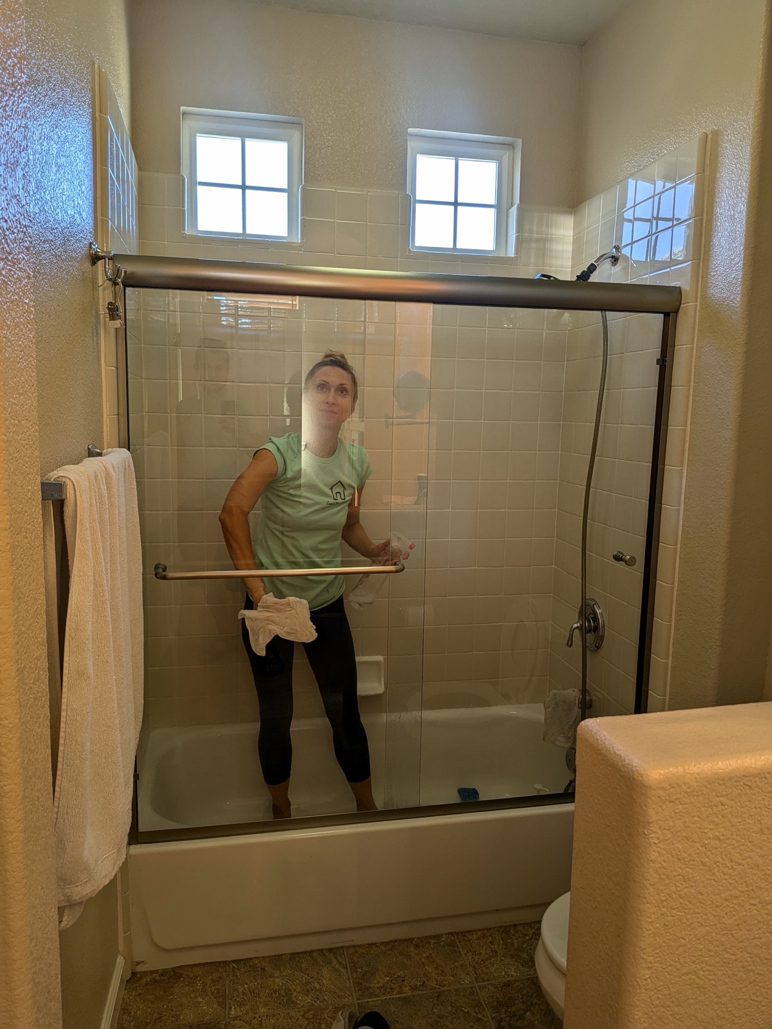 A cleaner squeegeeing a glass shower and tub enclosure