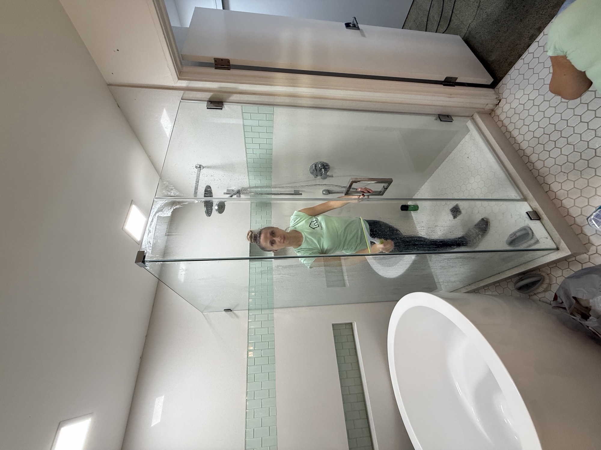 Crew member squeegeeing a new shower glass door after post-construction cleanup